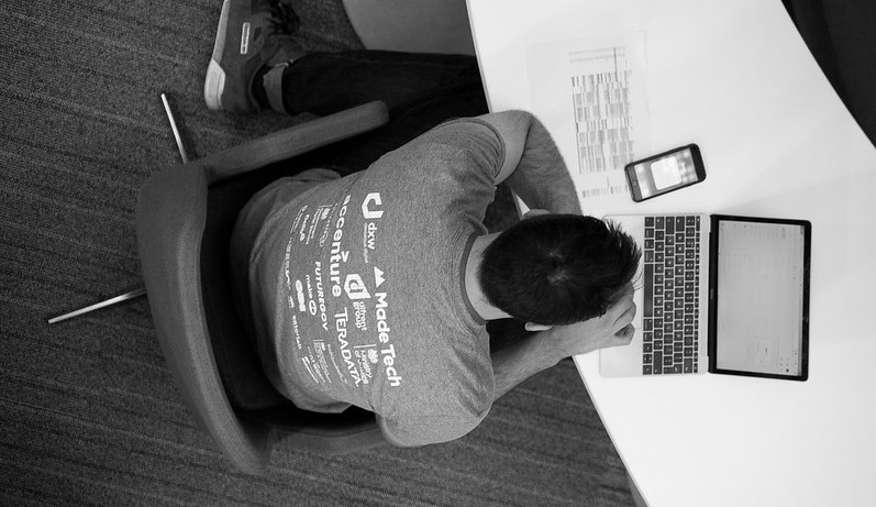 Attendee proudly wearing an event t-shirt with all the sponsor logo on the back while typing on a laptop
